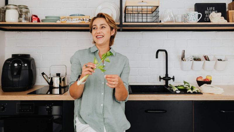 Smiling woman with vegetables in a stylish kitchen showcasing modern interior design.