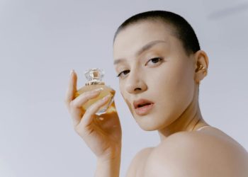 Close-up portrait of a woman with short hair holding a perfume bottle, showcasing elegance and style.