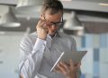 Professional man in eyeglasses focusing on tablet device in a stylish office setting.